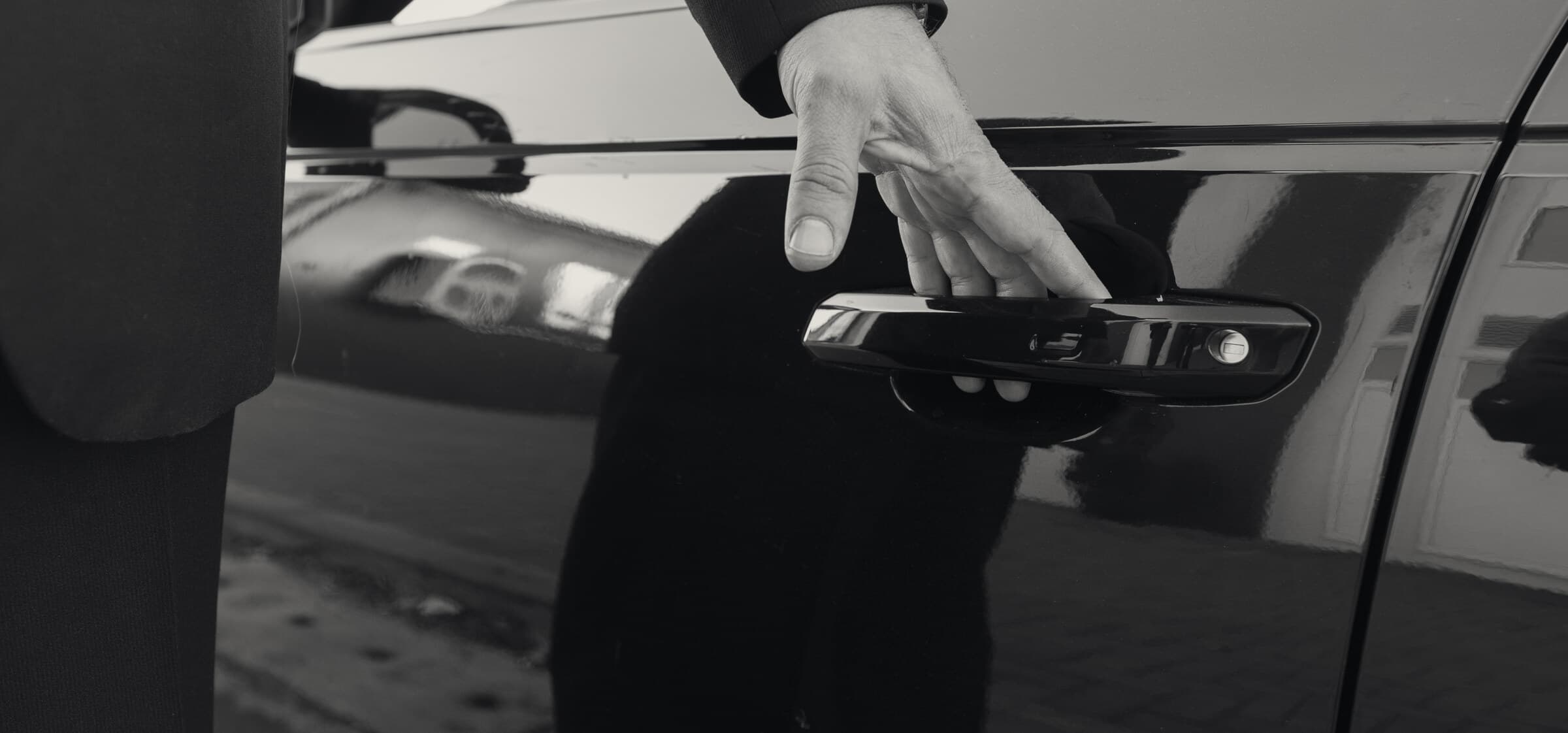 A chauffeur in a dark suit opening the rear door of a black car